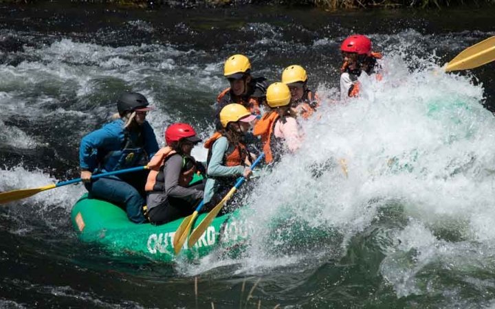 a group of gap year students navigate a raft through whitewater as a large wave hits the front of the raft